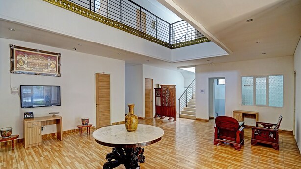 A spacious living area with a high ceiling, a wooden floor, a round table with a vase, a TV, and a staircase leading to an upper level. - OYO Life 91989 K24 Residence Syariah (Palembang)