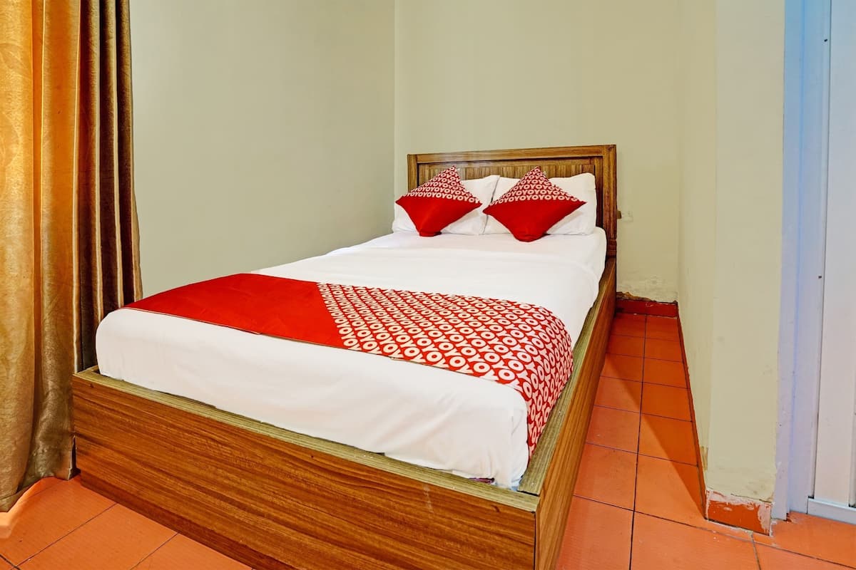 A single bed with a wooden frame, white bedding, and red accents.