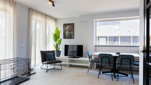 A modern living room with a TV, seating, a dining area, and a large window. - Spacious apartment for 4 people, with various facilities for your dog (Nieuwvliet-Bad)