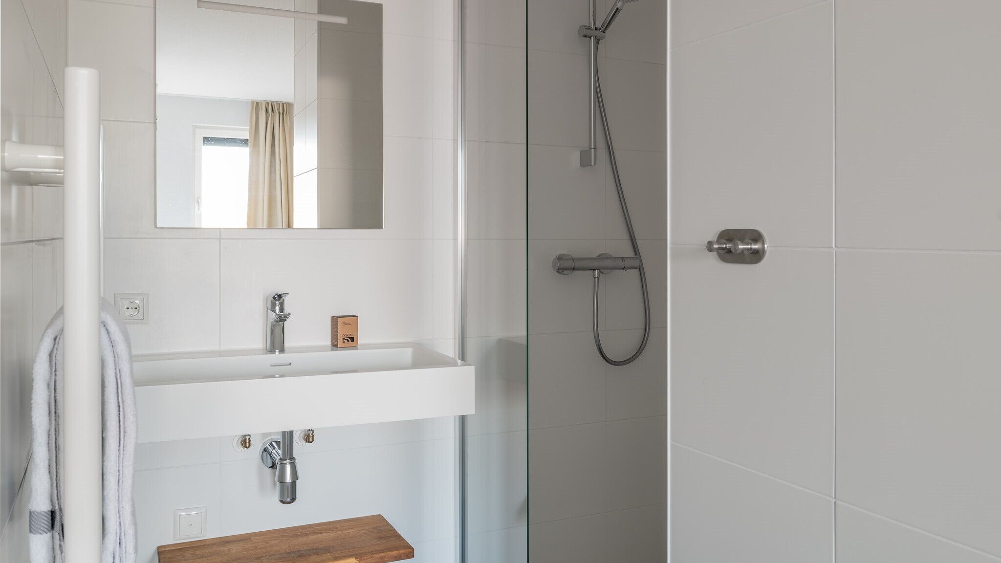 Une salle de bain moderne avec une douche à l’italienne en verre, un lavabo blanc doté d’un plan de toilette en bois et un miroir au-dessus du lavabo.