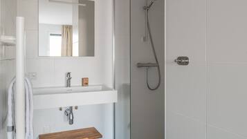 Une salle de bain moderne avec une douche à l’italienne en verre, un lavabo blanc doté d’un plan de toilette en bois et un miroir au-dessus du lavabo.
