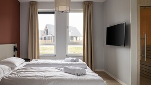 Ein Hotelzimmer mit einem Bett, zwei Fenstern, einem Fernseher und einer Holztür.
