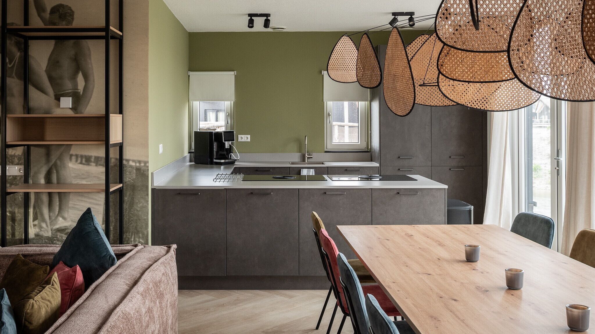 Een moderne keuken met een centraal eiland, een eetgedeelte met een houten tafel, en een zithoek met een bank en kussens.