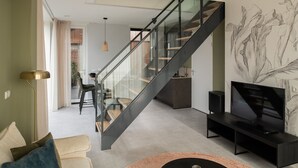 Un salon moderne doté d’un escalier en verre, d’un téléviseur à écran plat et d’un coin repas avec des chaises et une table.