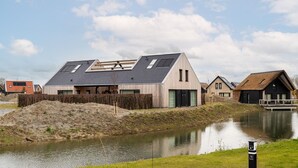 Une maison moderne avec un toit en pente, une clôture en bois et un petit étang au premier plan.