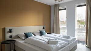 Hotelkamer met een groot bed, twee nachtkastjes, een hoofdeinde met wandlampen en uitzicht op het landschap door een groot raam.