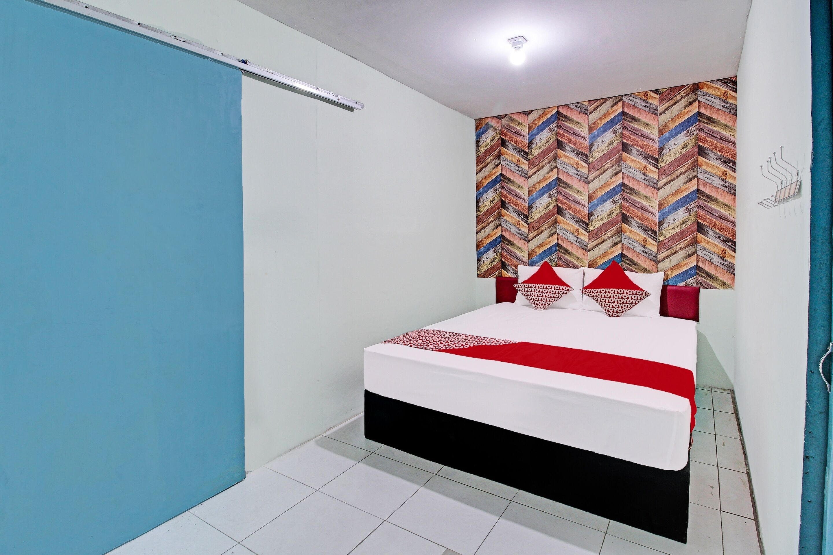 A bedroom with a bed, a blue wall, a white wall, a patterned wall, and a tiled floor.