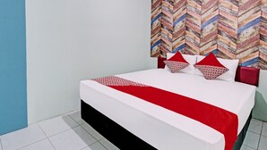 A bed with a white and red bedspread, two red pillows, and a patterned headboard.