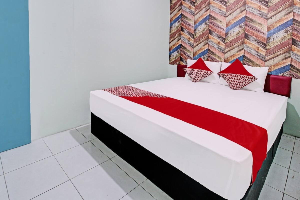 A bed with a white and red bedspread, two red pillows, and a patterned headboard.