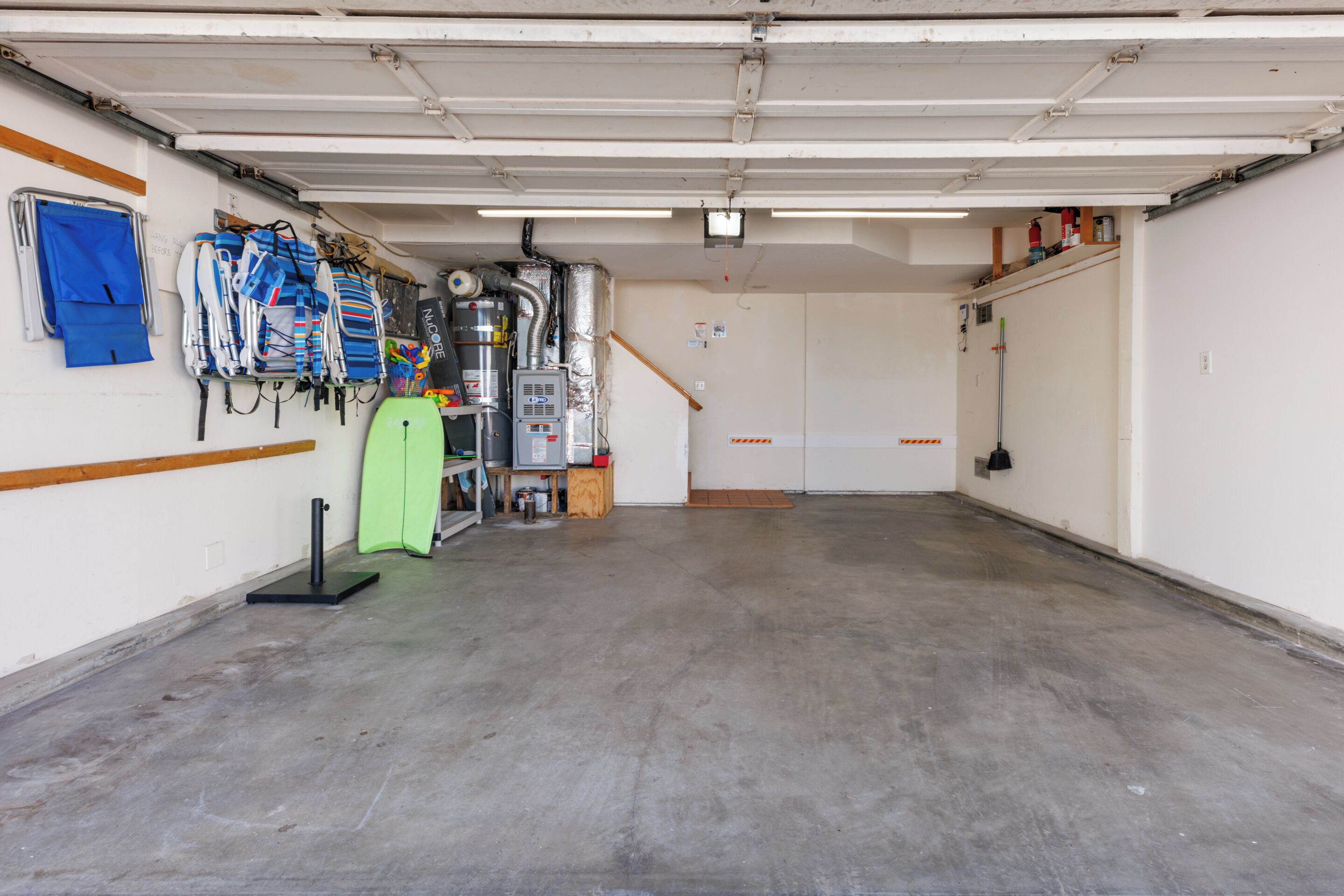 A garage with a concrete floor, a green surfboard, and a white wall with a window.