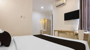 Una habitación de hotel con cama, escritorio, silla, televisor y aire acondicionado.