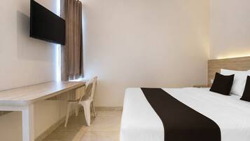 Habitación de hotel con cama, escritorio, silla, televisor de pantalla plana y ventana con cortinas.
