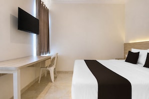 Habitación de hotel con cama, escritorio, silla, televisor de pantalla plana y ventana con cortinas.