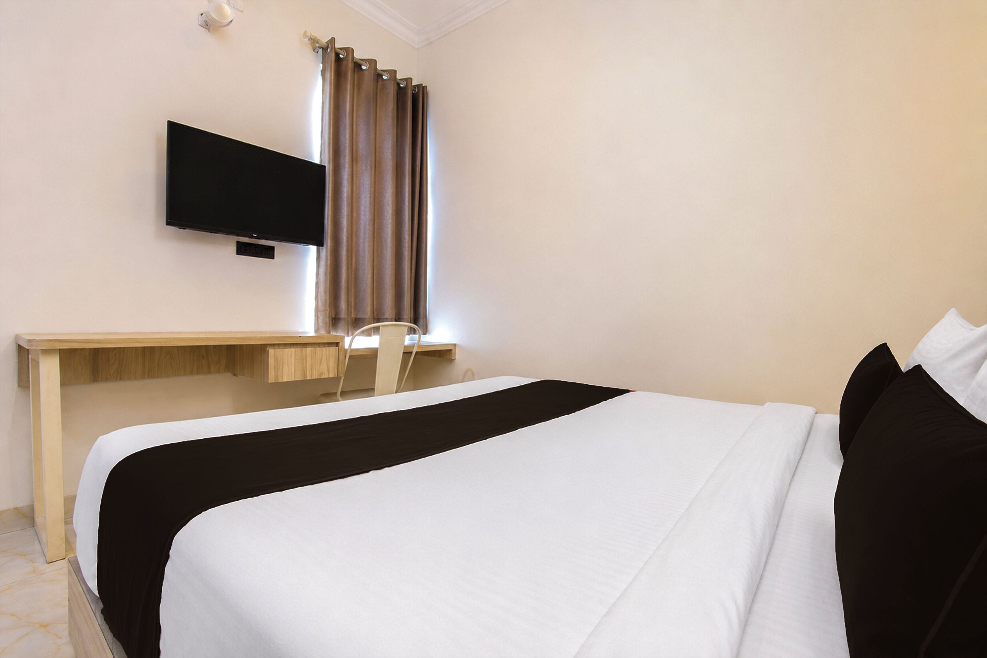 A hotel room with a bed, a desk, a chair, and a television mounted on the wall.