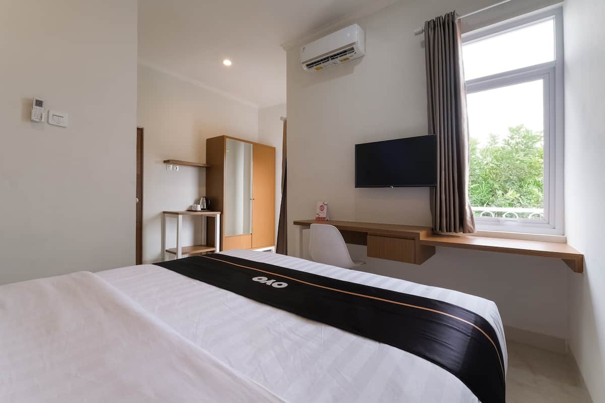 A hotel room with a bed, a desk, a chair, a television, an air conditioning unit, and a window with curtains.