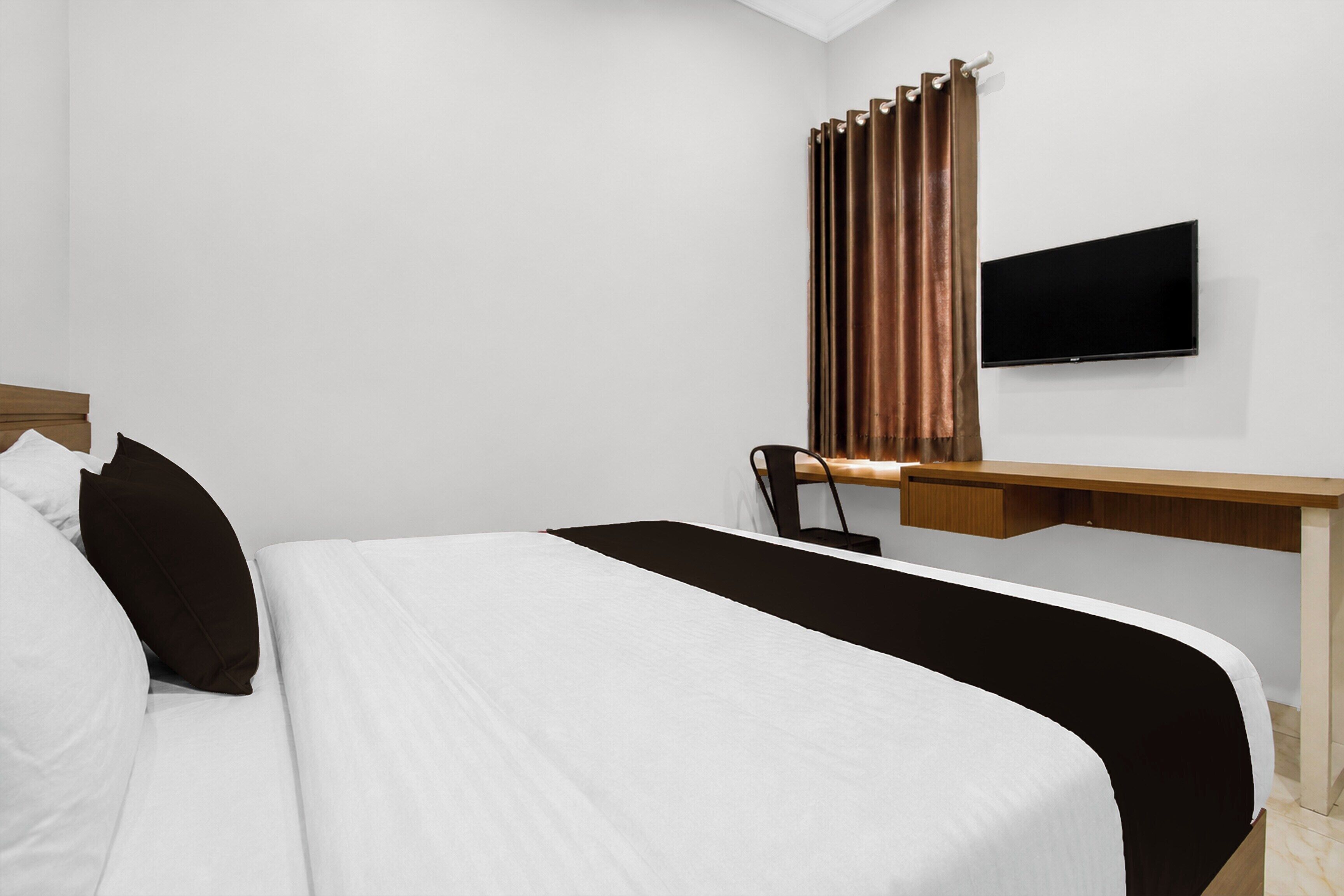 A hotel room with a bed, a desk, a chair, a television, and a window with curtains.