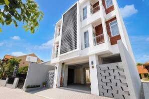 Un edificio moderno de varios pisos con fachada blanca, una entrada central y un área de estacionamiento techada.