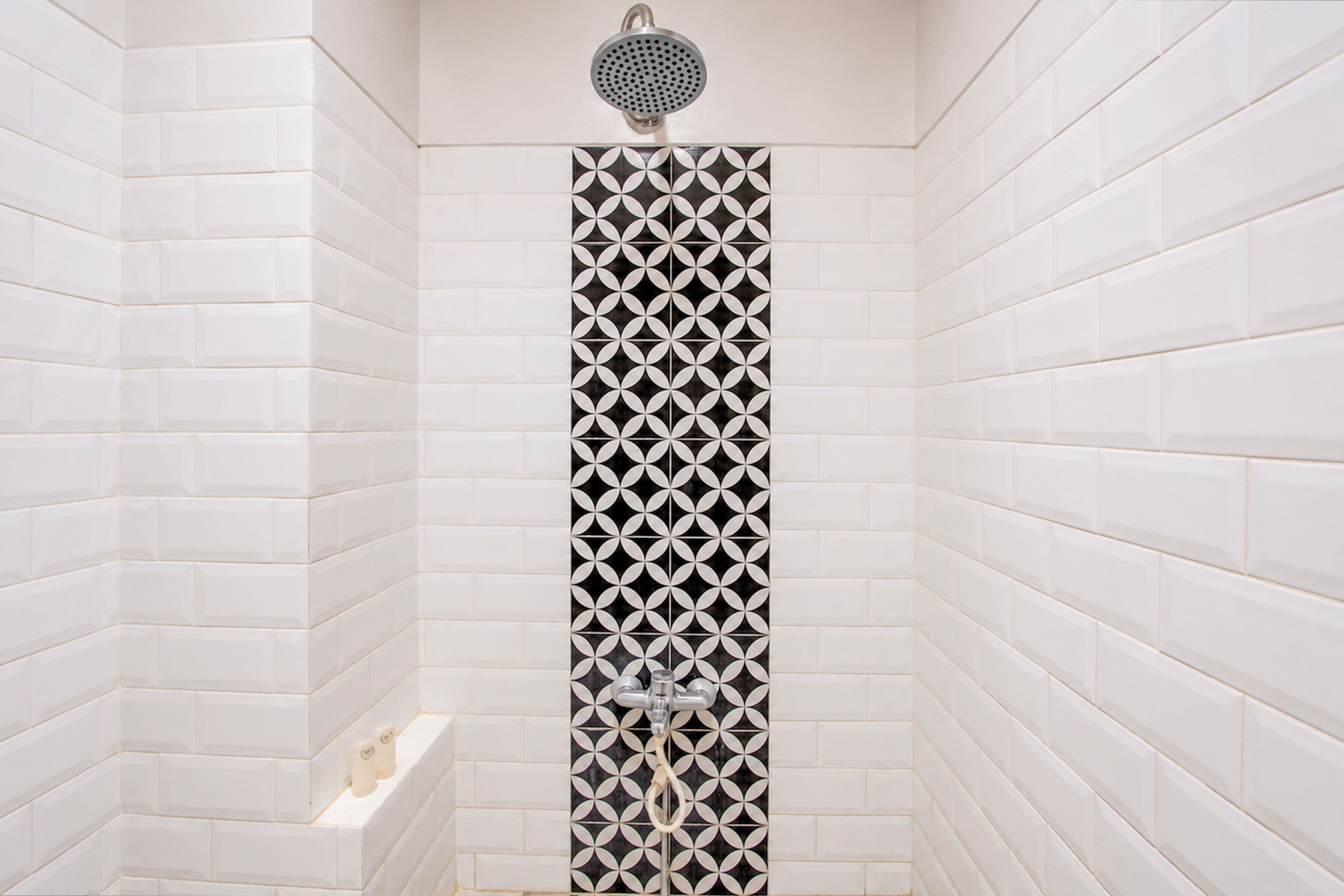 Una ducha con un patrón geométrico de azulejos, un cabezal de ducha manual y un pequeño estante con botellas.