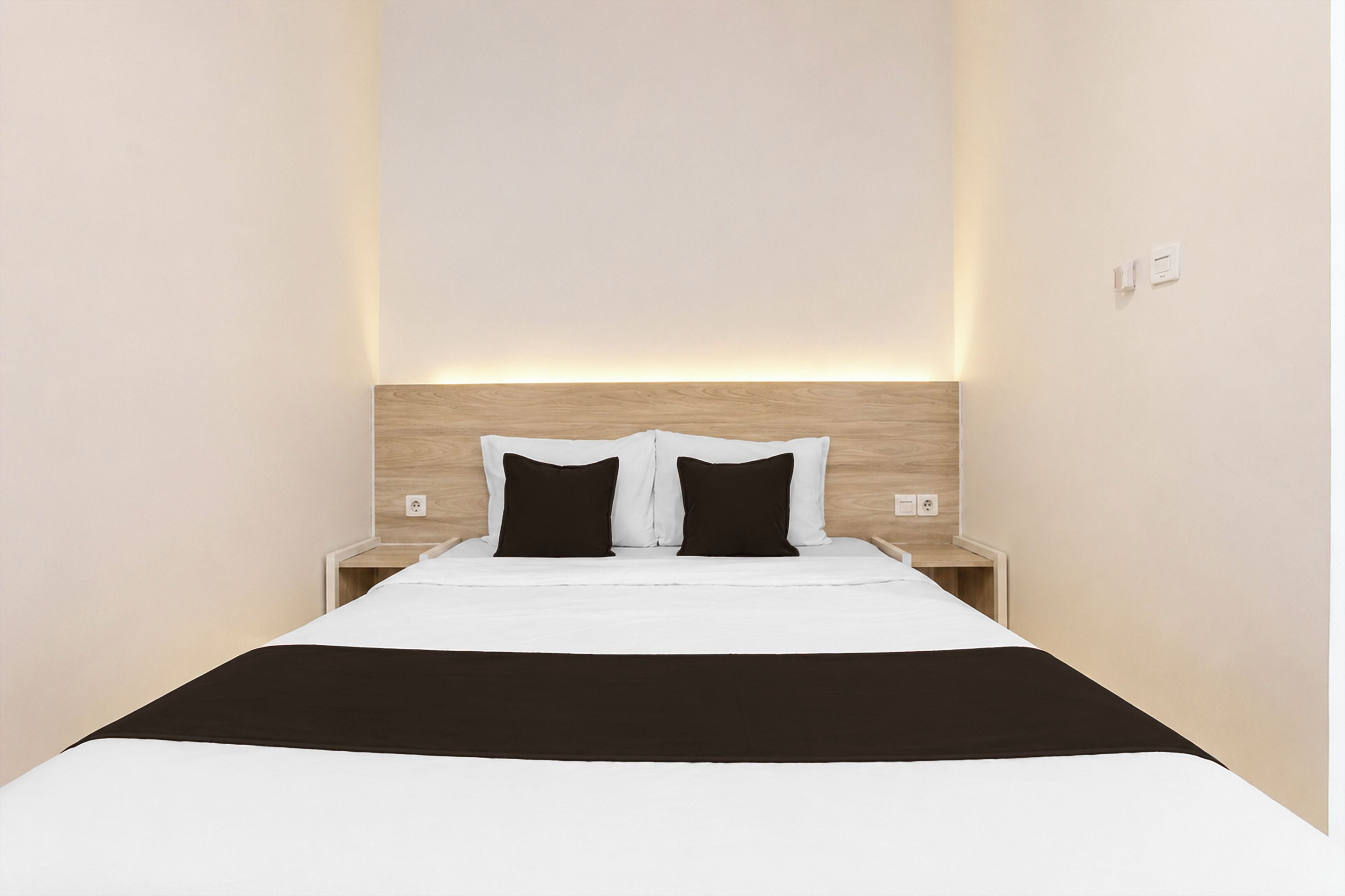 A narrow hotel room with a single bed, two bedside tables, and a wooden headboard.