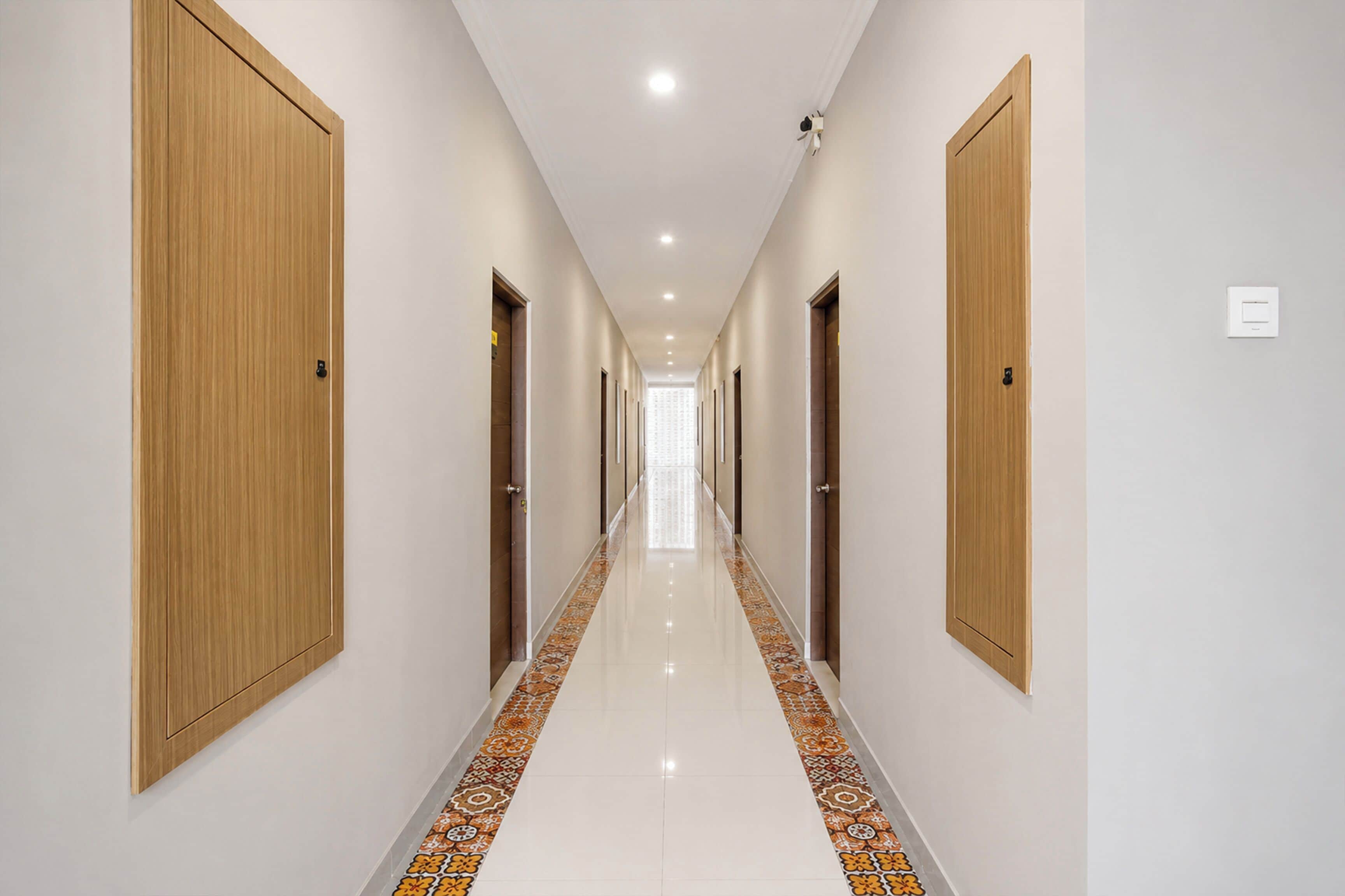 Un pasillo de hotel con puertas de madera, piso de baldosas y techo de color claro.
