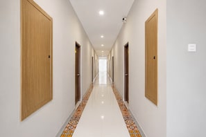 Un pasillo de hotel con puertas de madera, piso de baldosas y techo de color claro.