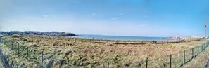 A coastal landscape with a fenced area, a distant town, and a clear sky.