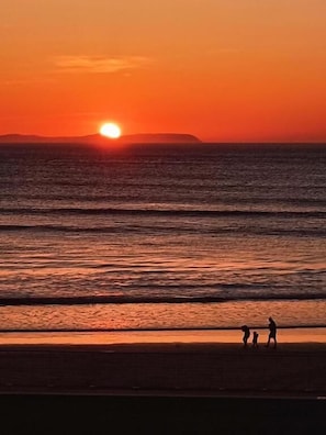 A sunset over the ocean with a beach and people walking.