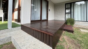 A modern outdoor patio with a wooden deck, a stone wall, and a glass door leading to a room. - Le Ciara (Randburg)