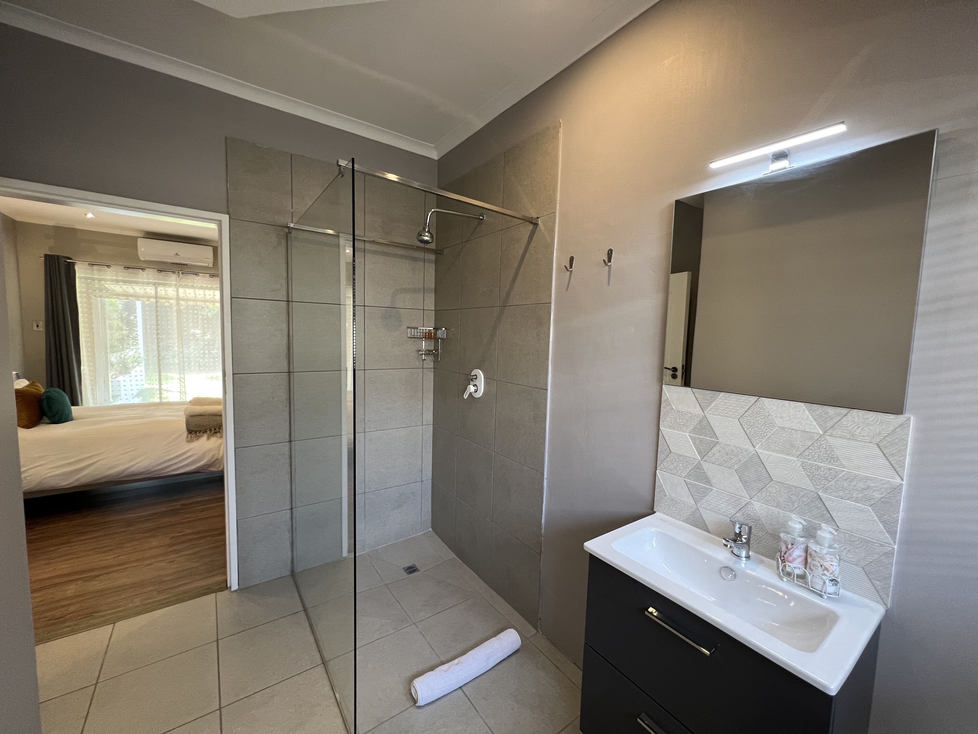 A modern bathroom with a glass shower enclosure, a white sink with toiletries, and a large mirror.