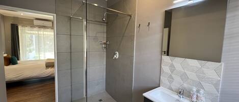 A modern bathroom with a glass shower enclosure, a white sink with toiletries, and a large mirror.