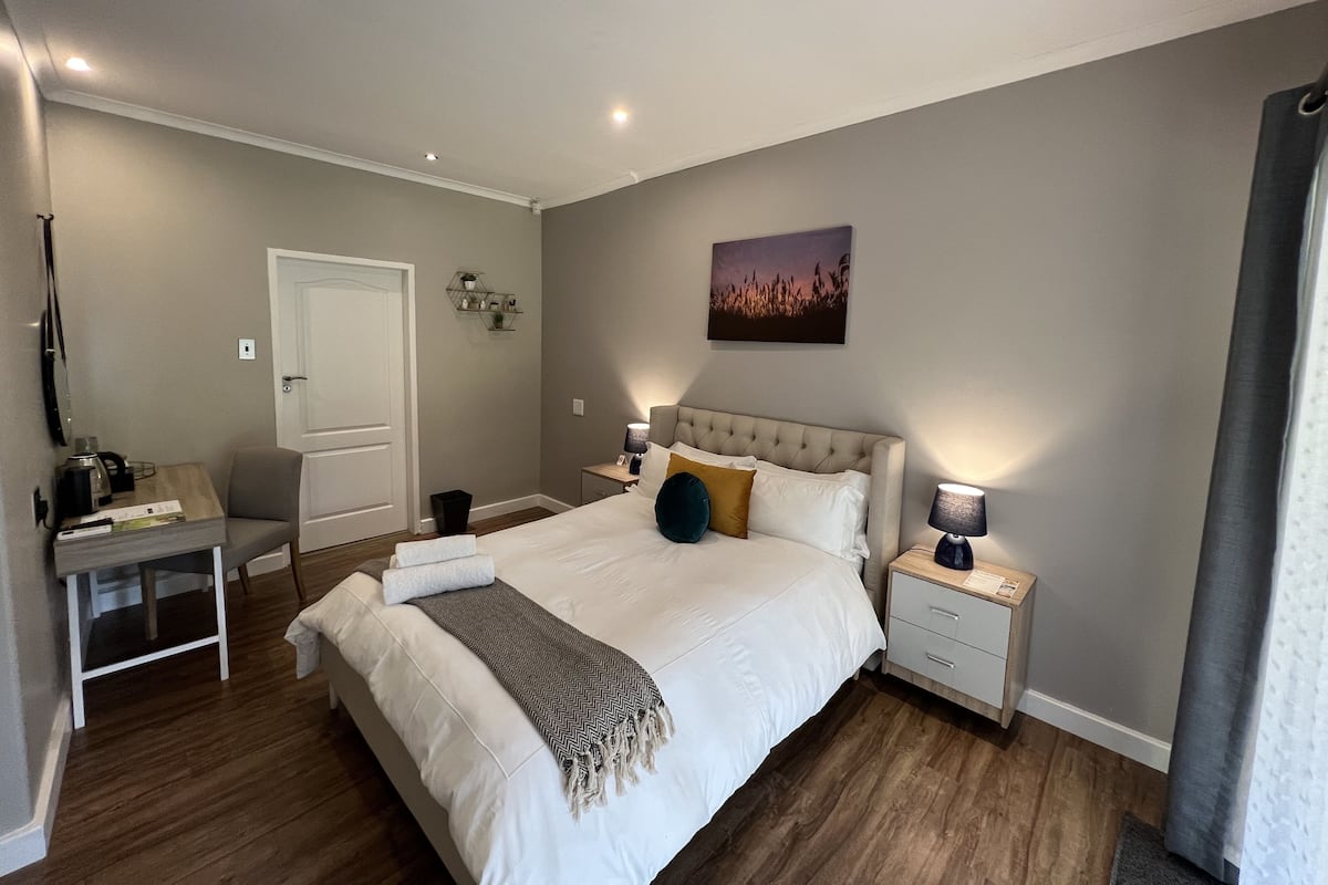 Un dormitorio moderno con una cama grande, mesitas de noche, un escritorio y una puerta.