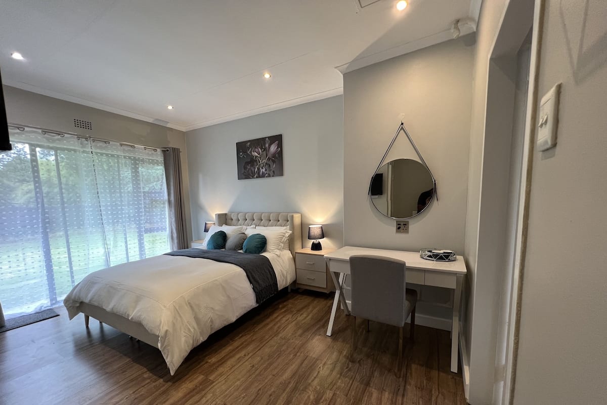 Un dormitorio con cama, mesita de noche, escritorio, silla y un espejo grande.