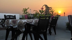 An outdoor dining area with a table set for four, surrounded by chairs, under a sunset sky. - Michaels Homestay (Jaipur)