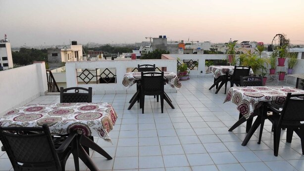 A rooftop terrace with multiple tables and chairs, surrounded by potted plants. - Michaels Homestay (Jaipur)