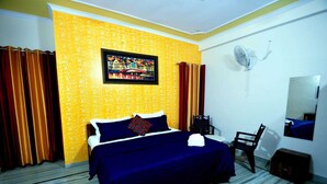 A hotel room with a bed, a chair, a fan, and a painting on the wall. - Michaels Homestay (Jaipur)