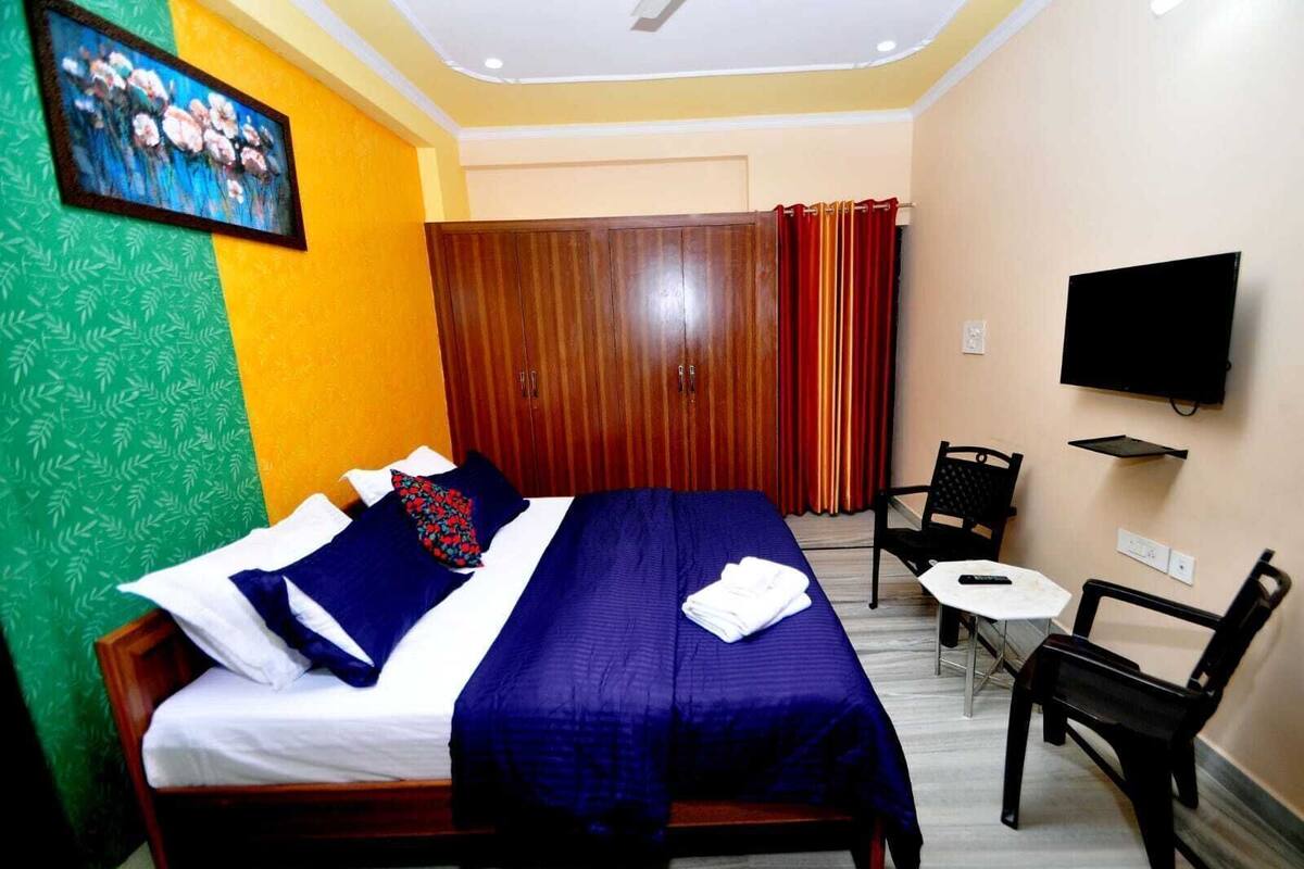 Habitación de hotel con cama, escritorio, silla, televisor y ventana con cortinas.
