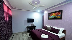 A hotel room with a bed, a desk, a chair, a television, and a ceiling fan. - Michaels Homestay (Jaipur)
