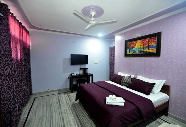 A hotel room with a bed, a desk, a chair, a television, and a ceiling fan.