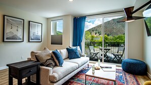 Una sala de estar moderna con sofá, una mesita de centro y vistas a montañas a través de grandes ventanales.