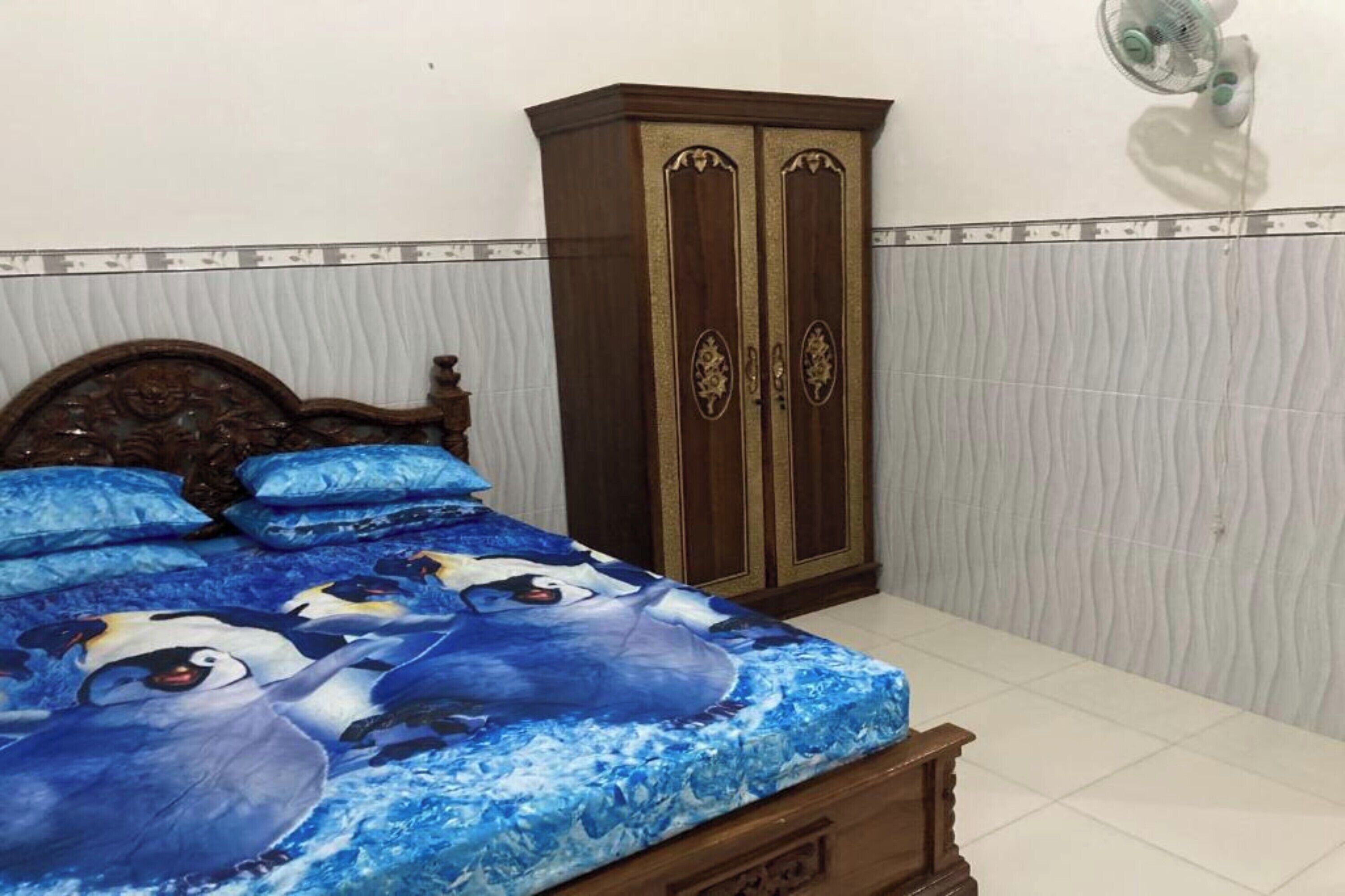 A bedroom with a bed, a wardrobe, and a wall-mounted fan.