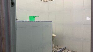 Un baño pequeño con azulejos, un inodoro, un balde verde y una zona de ducha con un estampado azul y blanco.