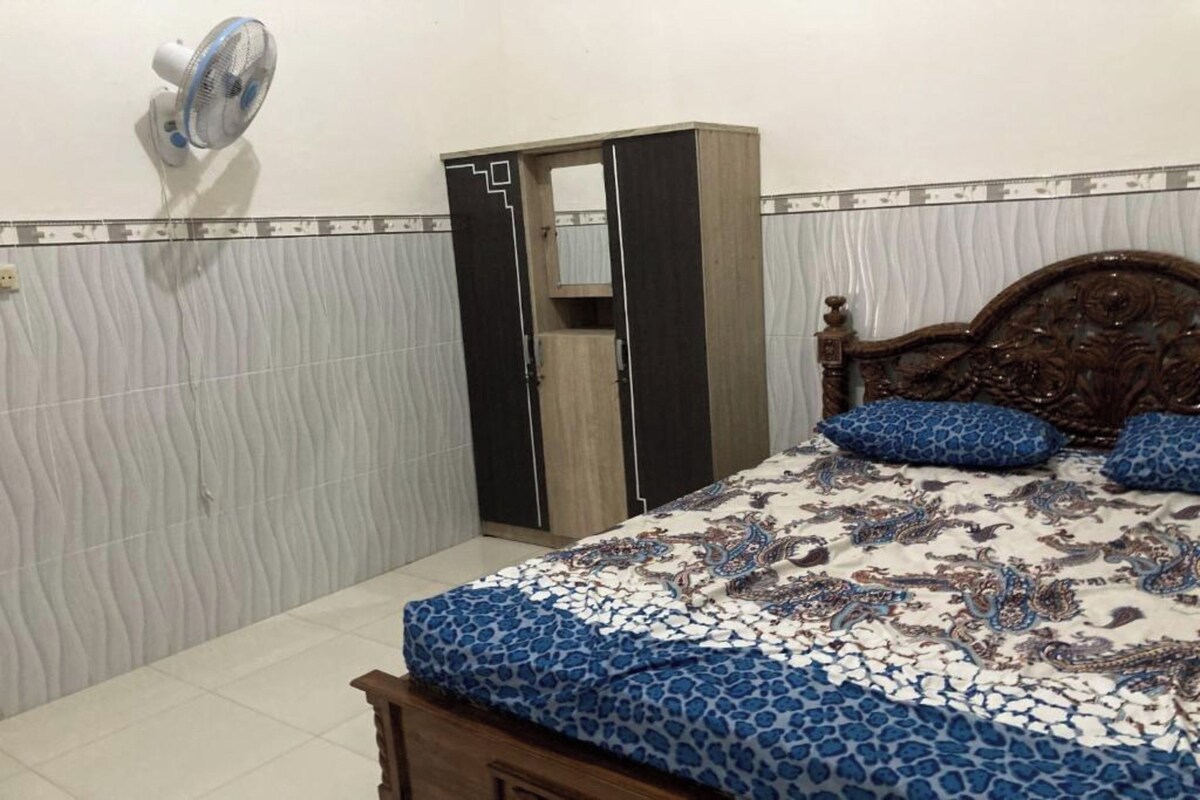 Un dormitorio con cama, armario y ventilador en la pared.