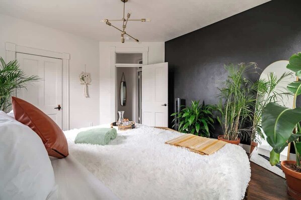 A bedroom with a fluffy white bed, a wooden side table, and a black accent wall.