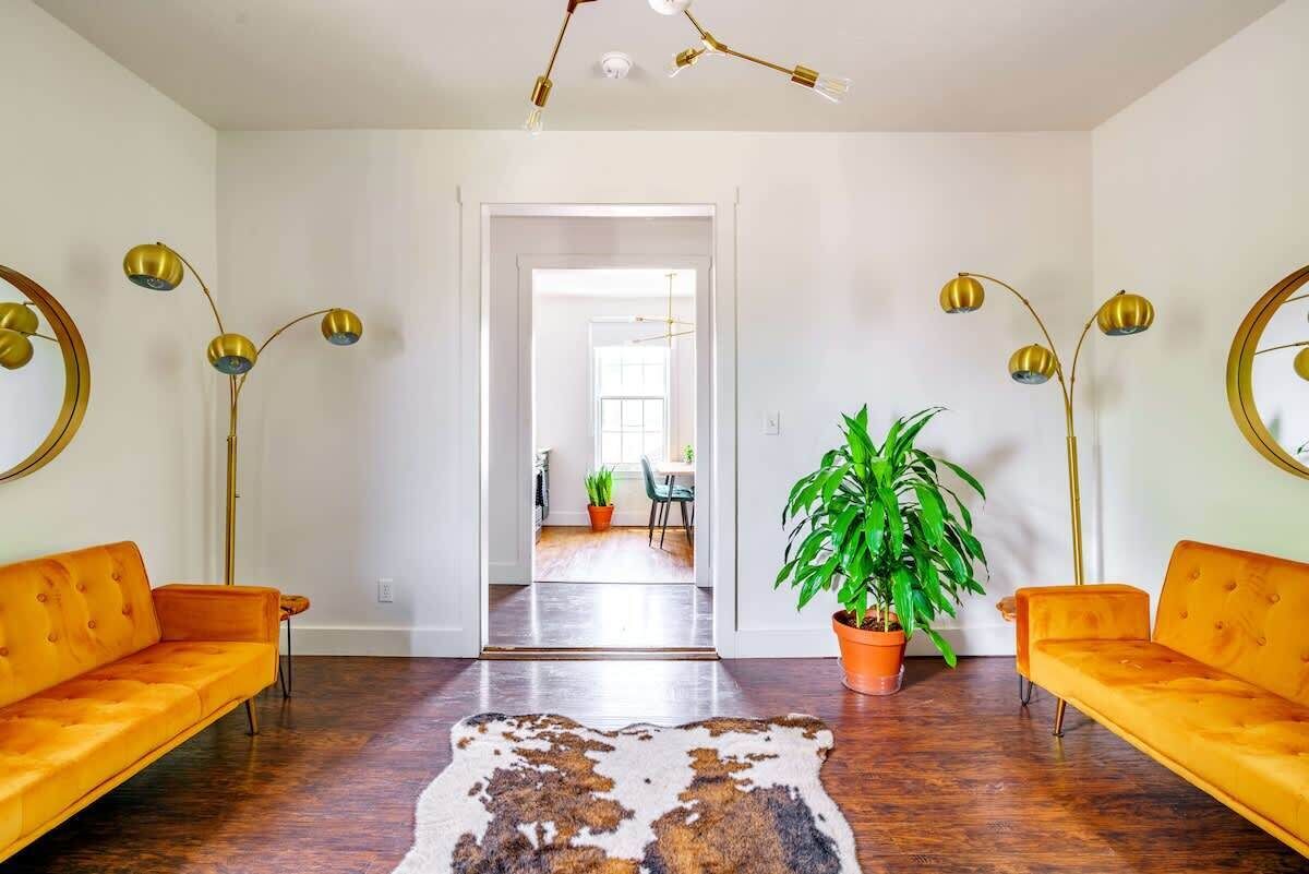 Un salon moderne avec un tapis en peau de vache, deux canapés orange, une plante en pot et des lampadaires dorés.
