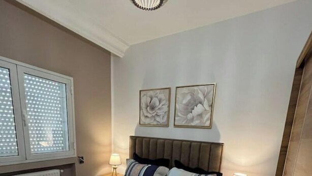 A bedroom with a bed, two bedside lamps, a window with blinds, and two wall-mounted flower paintings. - Sweet Appart Centre Urbain Nord Aéroport Annul Flex (Tunis)