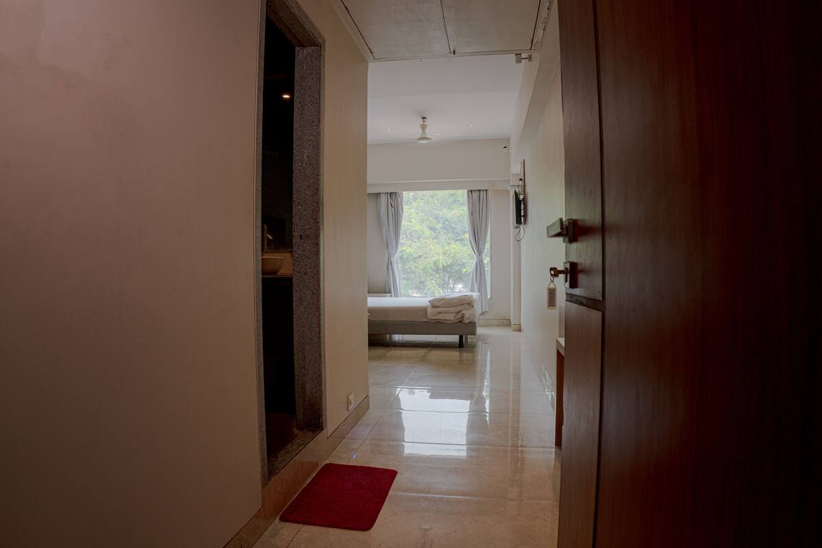 A hallway leading to a bedroom with a bed, a red mat, and a window with curtains.