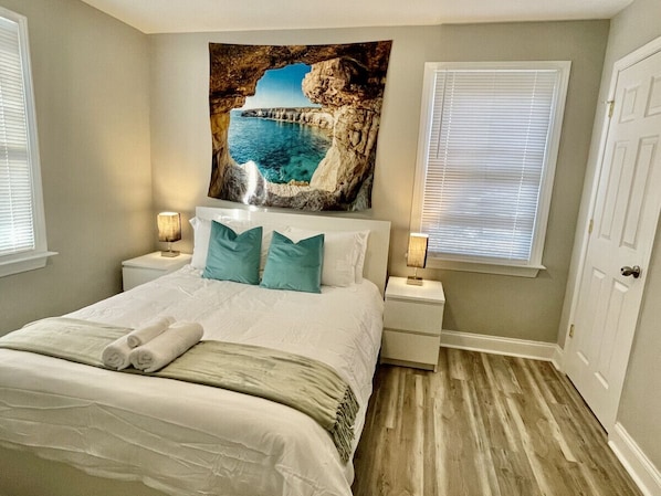 Une chambre à coucher avec un lit, deux tables de chevet, un tableau et une porte.