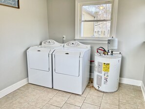 A laundry room with two stacked front-loading washers and a water heater. - Vibrant 3BR Ranch | Prime Greensboro Location (Greensboro)