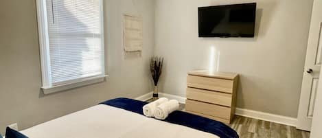 A bedroom with a bed, a dresser, a flat-screen TV, and a window with blinds.