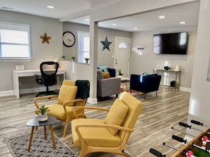 Un salon moderne avec un bureau, deux fauteuils jaunes, un canapé gris et un téléviseur.